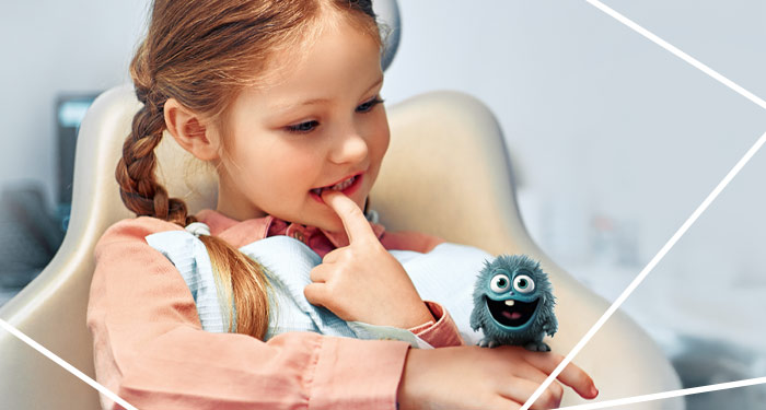 Kleines Mädchen auf dem Behandlungsstuhl auf deren Finger ein kleines niedliches blaues Monster sitzt